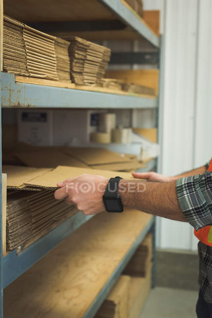 Sección media del hombre que arregla el cartón en el estante - foto de stock
