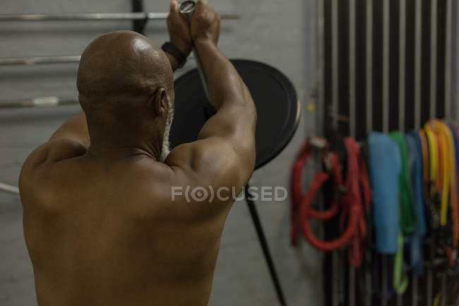 Rear view of man exercising with barbell in fitness studio. — Stock Photo