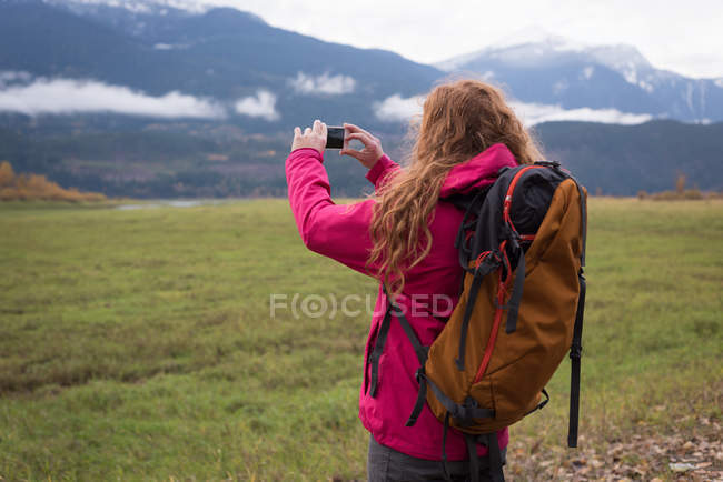 Primo piano di donna con zaino che fotografa montagne innevate — Foto stock