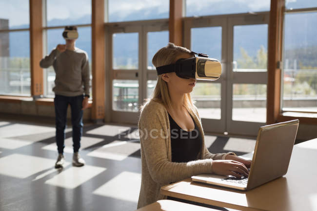 Estudantes universitários usando laptop e fone de ouvido de realidade virtual à mesa — Fotografia de Stock
