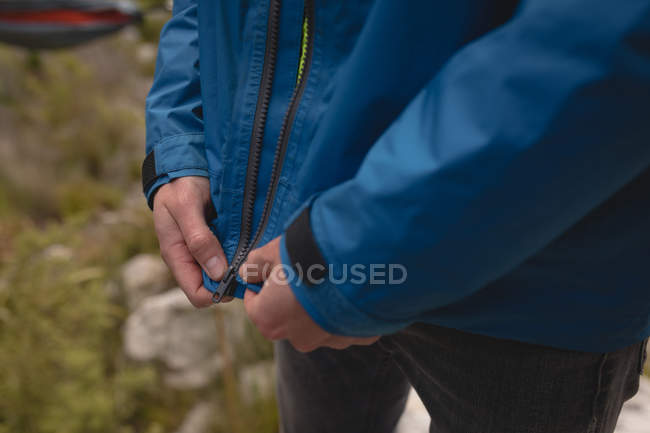 Primer plano de la mano excursionista tirando de la cremallera de la chaqueta impermeable de lluvia - foto de stock