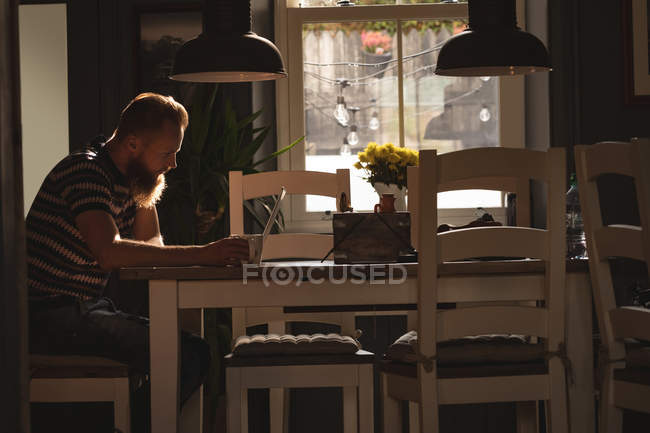 Человек сидит на стуле, используя свой ноутбук дома — стоковое фото