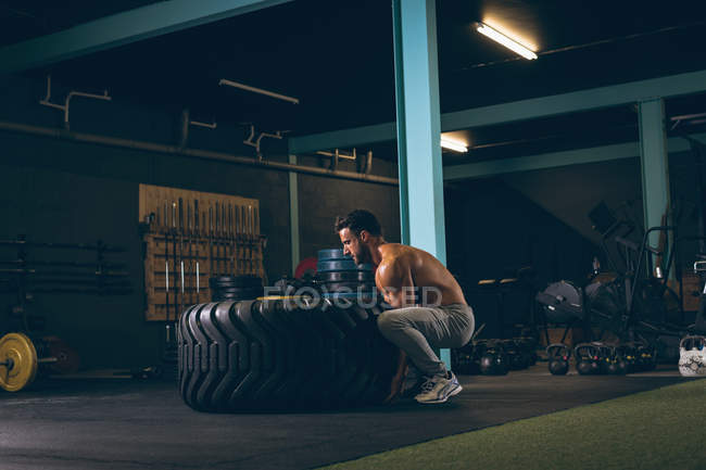 Мускулистый мужчина тренируется с тяжелой шиной в фитнес-студии — стоковое фото