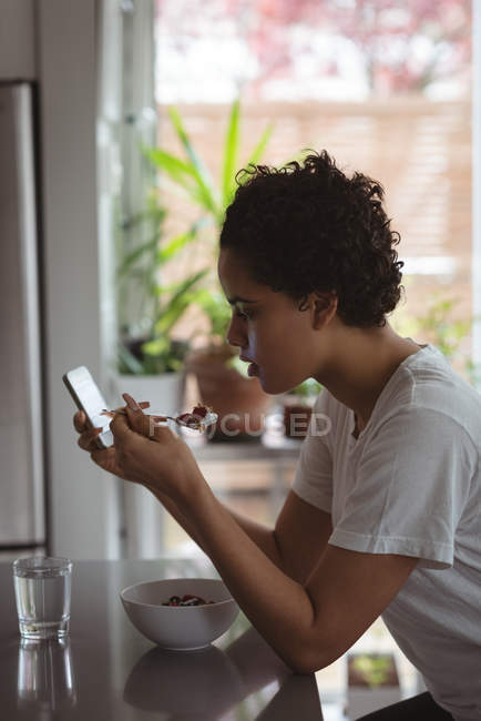 Frau frühstückt zu Hause mit Handy — Stockfoto