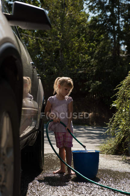 Дівчина наповнює воду у відрі під час прання автомобіля — стокове фото