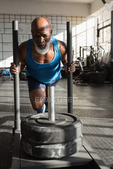 Homem sênior determinado empurrando trenó de peso no estúdio de fitness . — Fotografia de Stock