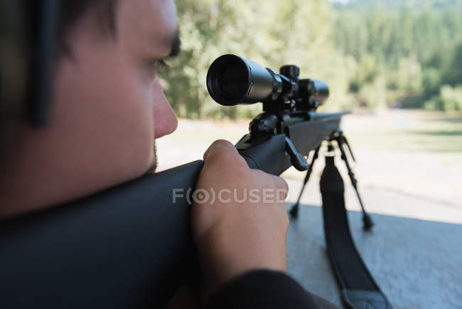 Hombre apuntando rifle de francotirador al objetivo en el campo de tiro en un día soleado - foto de stock