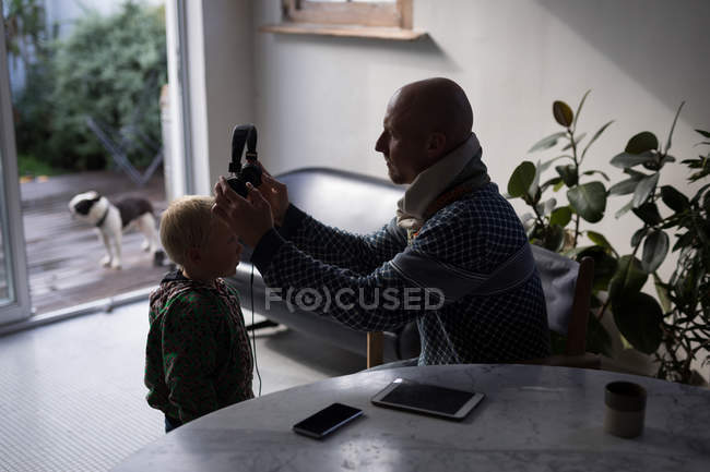 Father putting headphones on boy at home. — Stock Photo