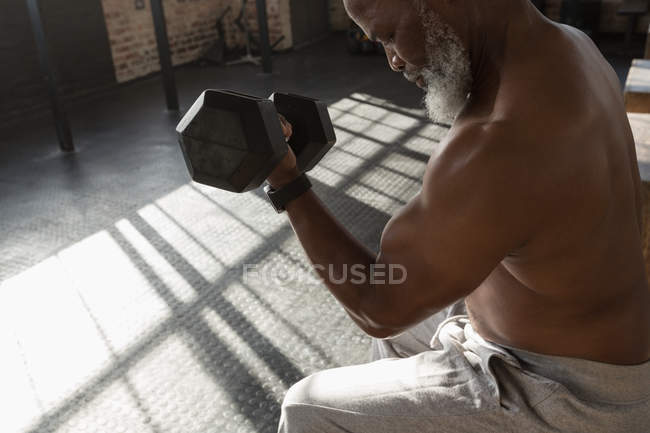 Close-up of determined senior man exercising with dumbbell in fitness studio. — Stock Photo