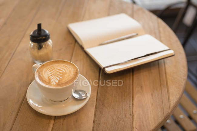 Tazza di cappuccino con diario sul tavolo in caffetteria — Foto stock