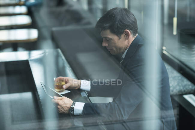Businessman using digital tablet while having whisky at hotel counter — Stock Photo