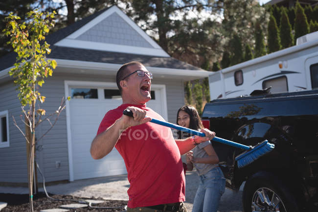 Padre e hija se divierten mientras lavan el coche en el garaje exterior - foto de stock