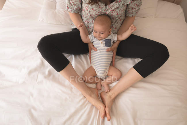 Cute little baby between mother legs on bed at home — Stock Photo