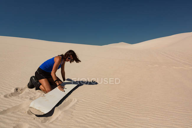 Mujer aplicando cera de tabla de surf al sandboard en el desierto en un día soleado - foto de stock