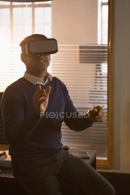 Улыбающийся бизнесмен, использующий гарнитуру виртуальной реальности в офисе . — стоковое фото