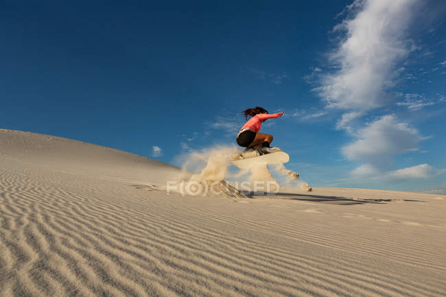 Mujer haciendo sandboard en una duna de arena en el desierto - foto de stock