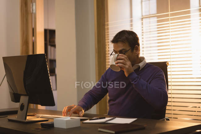Бізнесмен п'є каву, використовуючи настільний комп'ютер за столом в офісі . — стокове фото