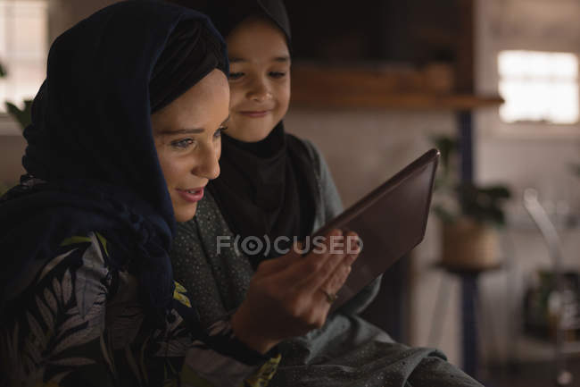 Sonriente madre e hija musulmana usando tableta digital - foto de stock