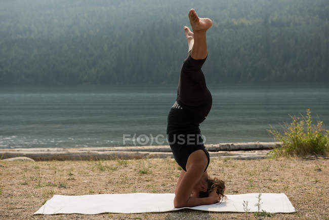 Sporty woman practicing head stand near the sea coast on a sunny day — Stock Photo