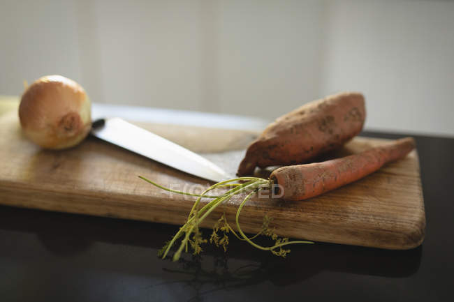 Close-up de faca, cenoura e cebola na tábua de cortar — Fotografia de Stock