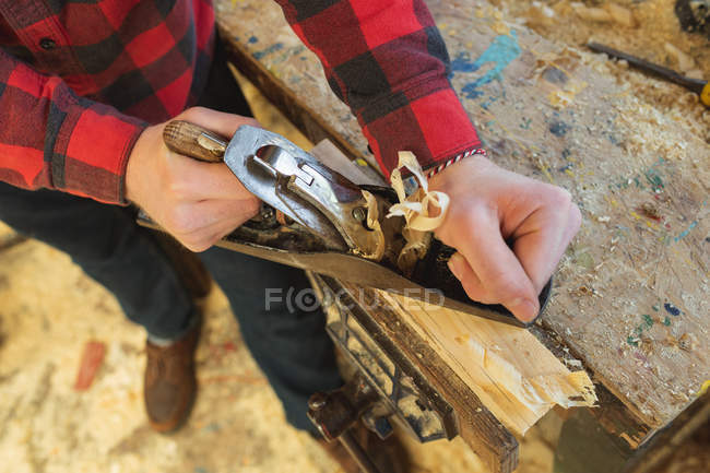 Primer plano del carpintero masculino utilizando una herramienta plana en el taller - foto de stock