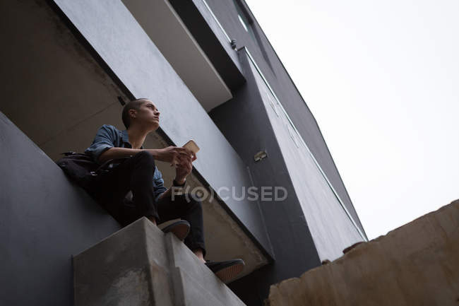 Задуманный молодой человек, сидя на балконе, пользуется мобильным телефоном — стоковое фото