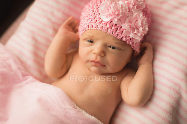 Newborn baby in knitted hat relaxing on baby bed at home. — Stock Photo