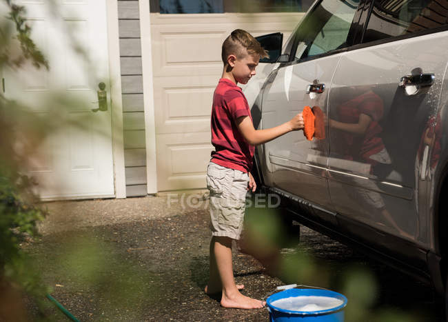 Junge wäscht an einem sonnigen Tag sein Auto in der Garage — Stockfoto