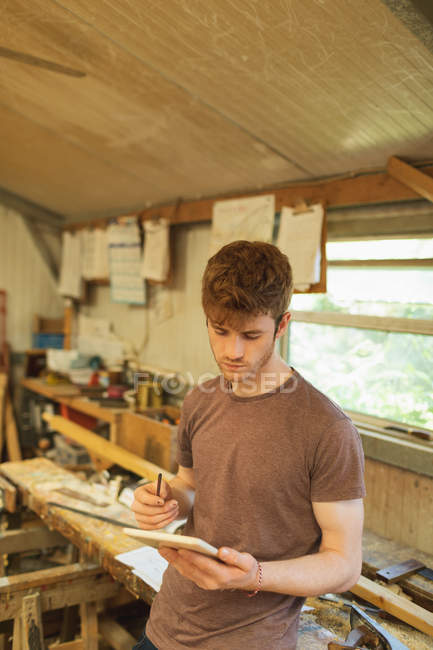 Jovem carpinteiro masculino usando tablet digital em oficina — Fotografia de Stock