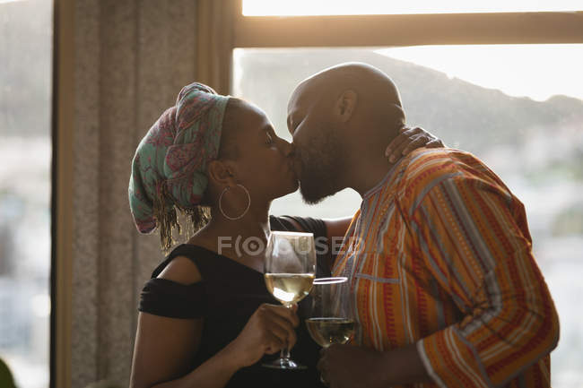 Пара цілується, маючи вино біля вікна вдома . — стокове фото