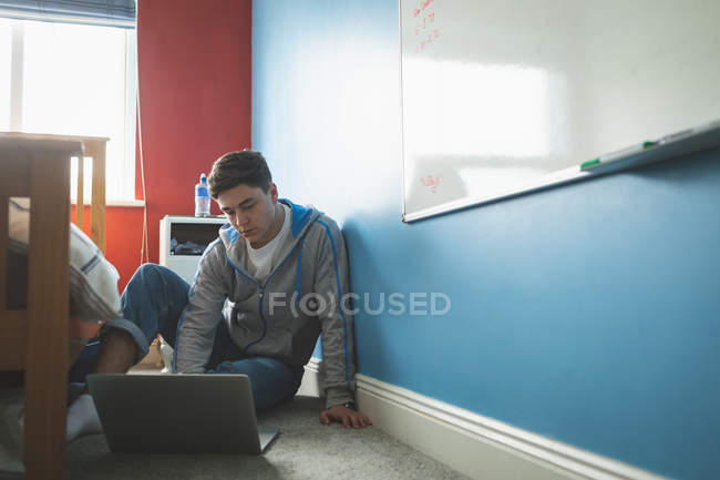 Giovane uomo che lavora con il computer portatile mentre seduto sul pavimento in camera da letto . — Foto stock