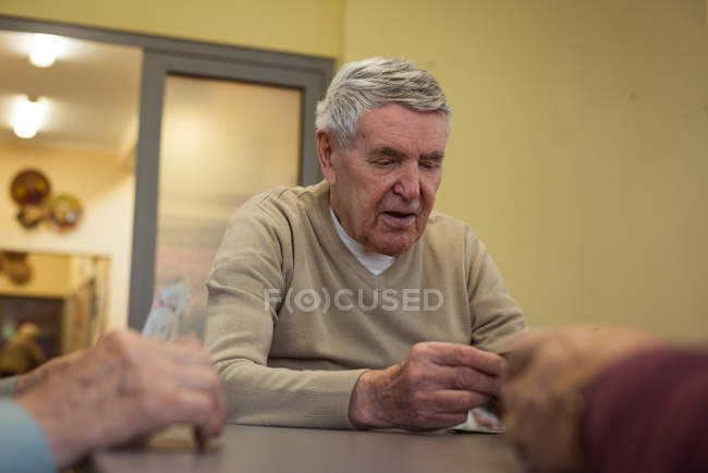 Старший чоловік грає в карти в будинку престарілих — стокове фото