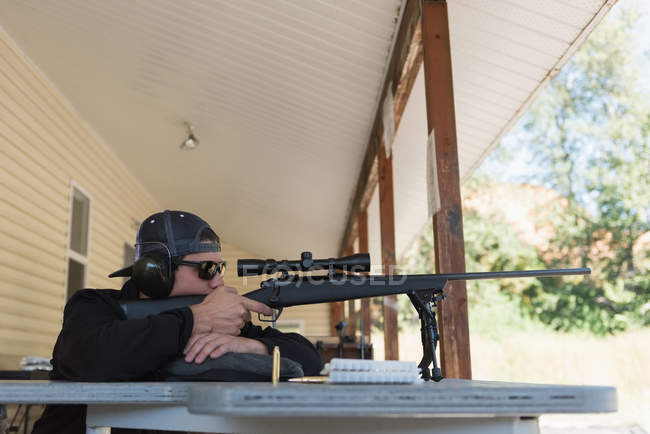 Hombre apuntando rifle de francotirador al objetivo en el campo de tiro en un día soleado - foto de stock