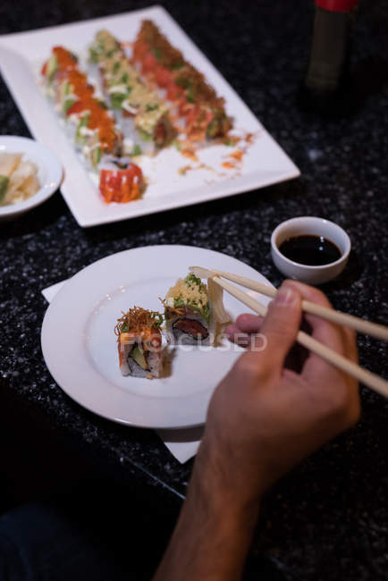 Hombre recogiendo sushi con palillos en un restaurante - foto de stock