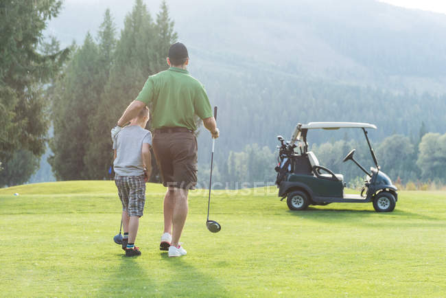 Вид ззаду батька і сина, що йде з гольф-клубом на трасі — стокове фото