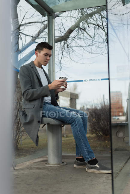 Homme utilisant un téléphone portable tout en prenant un café à l'arrêt de bus — Photo de stock