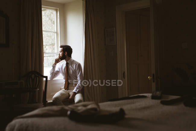 Задумчивый мужчина смотрит из окна на дом — стоковое фото