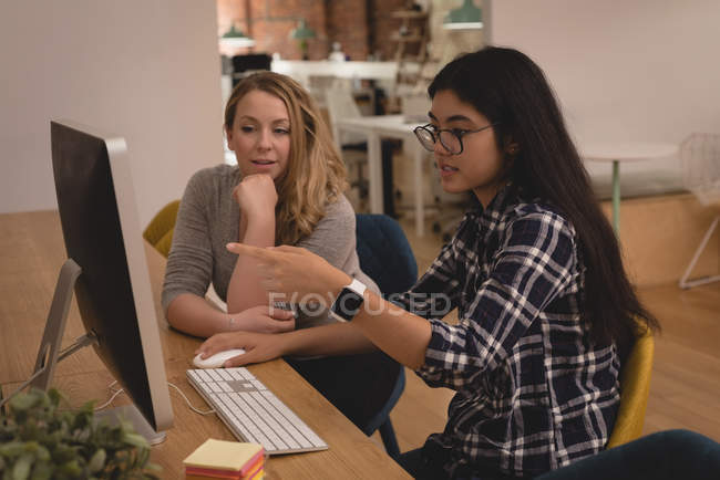 Ejecutivas discutiendo por computadora en la oficina creativa - foto de stock
