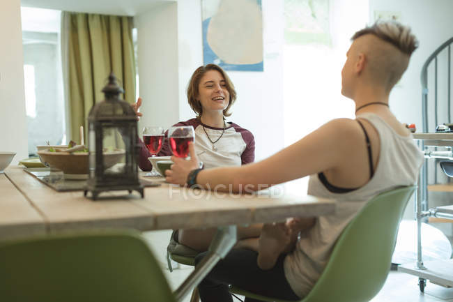 Mujeres jóvenes cenando con copas de vino tinto en la moderna sala de estar . - foto de stock