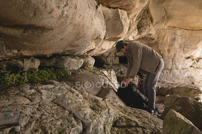 Caminhante checando sua mochila dentro da caverna em um dia ensolarado — Fotografia de Stock