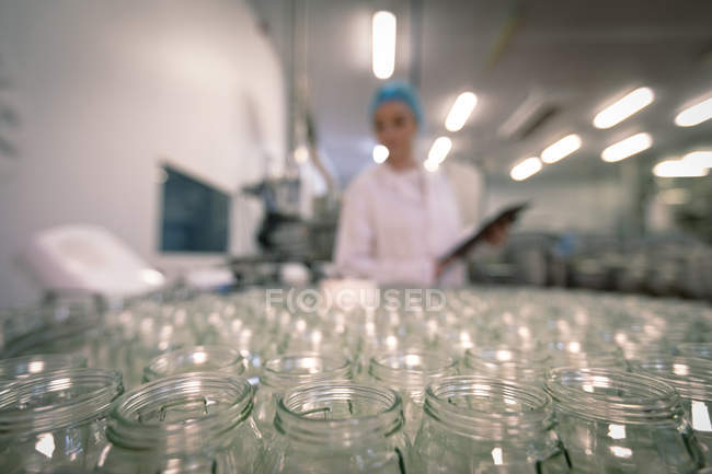 Женщина-работница наблюдает за стеклянными банками на производственной линии на заводе — стоковое фото