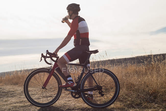 Горный велосипедист пьет воду в сельской местности в солнечный день — стоковое фото
