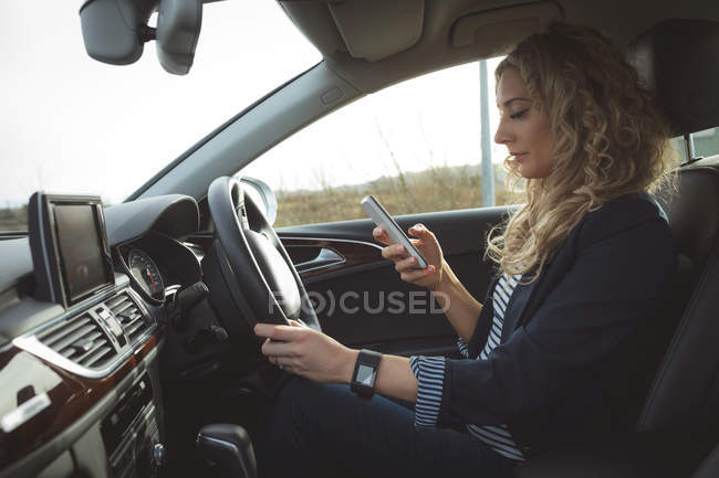 Belle femme exécutive utilisant le téléphone portable tout en conduisant dans une voiture — Photo de stock
