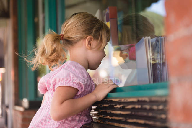 Girl peeping through the glass window outside the book store — Stock Photo