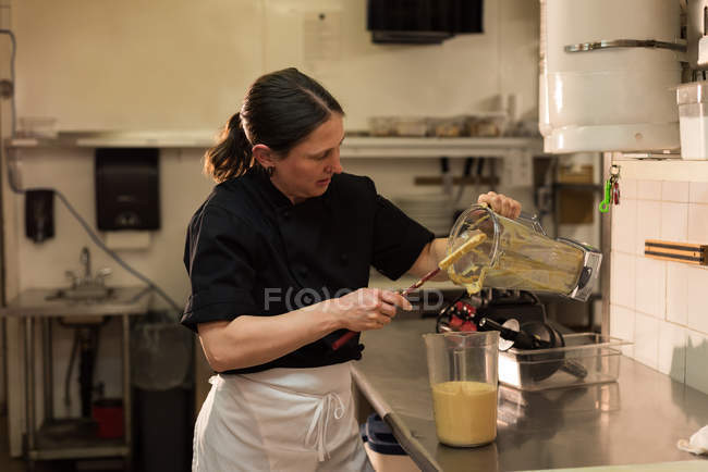 Chef emptying a ground paste in a container at commercial kitchen — Stock Photo