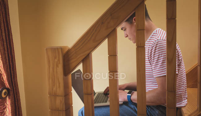 Hombre usando portátil en escalera de madera en casa
. - foto de stock