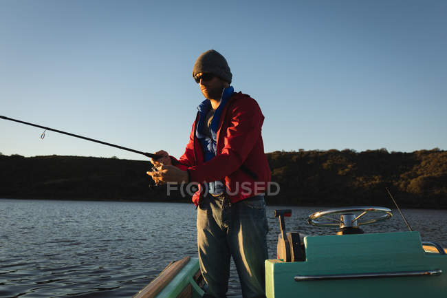 Человек рыбачит, стоя на моторной лодке в реке . — стоковое фото