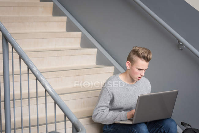 Teenage boy using laptop on staircase in university — Stock Photo