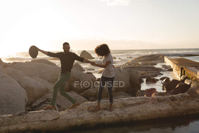 Romantica coppia che cammina sulla roccia vicino a una spiaggia nella giornata di sole — Foto stock