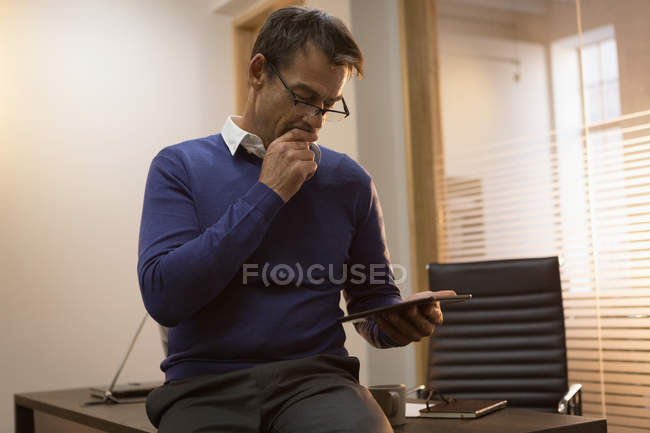 Empresário usando tablet digital enquanto sentado na mesa no escritório . — Fotografia de Stock
